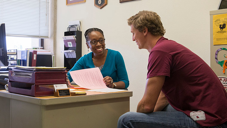 A professor talks to a student in her office during an advisement session.