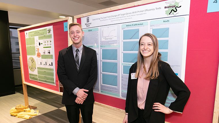 Two students posing in front of their research poster at the CNAS Undergraduate Research Symposium.