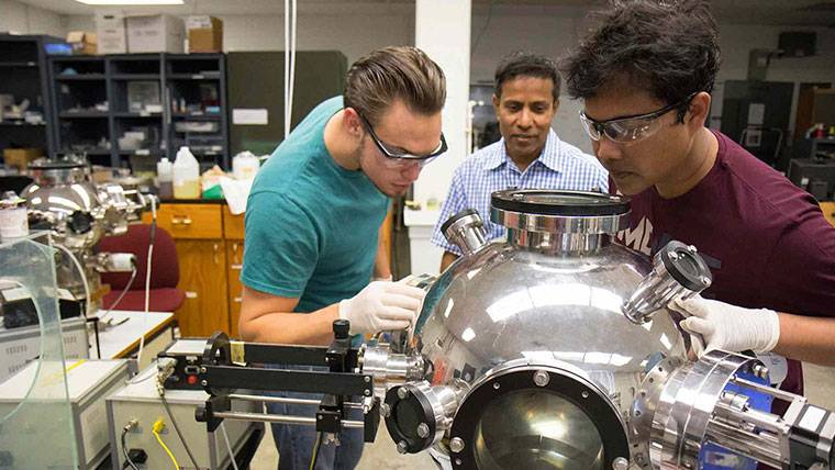 Graduate students and Dr. Kartik Ghosh work with pulsed laser deposition.