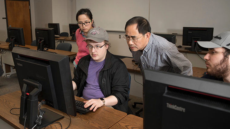 Missouri State student looking at a computer monitor in a classroom while others look over their shoulder. 