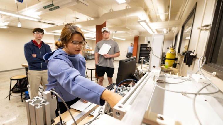 A mechanical engineering student connects wires to a machine during a lab session.